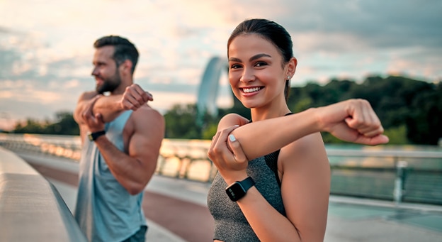 Man and woman stretching arms on a footbridge outdoors during an early morning workout session