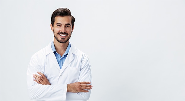 Smiling male doctor in a white lab coat standing with arms crossed against a neutral background.