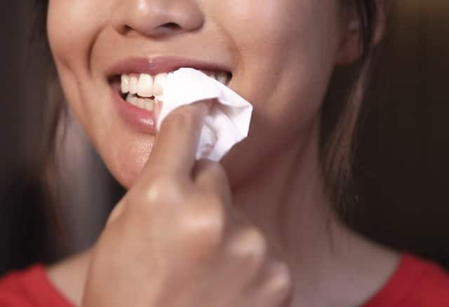 Lady drying her teeth with tissue 