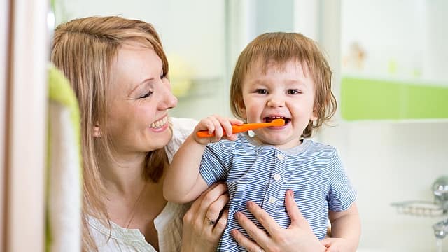 mother is helping her kid brushing teeth to prevent tooth decay